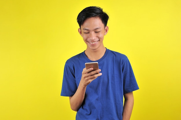 Heureux de beau jeune homme asiatique souriant à l'aide de smartphone isolé sur fond jaune