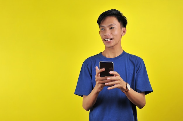 Heureux de beau jeune homme asiatique souriant à l'aide de smartphone isolé sur fond jaune