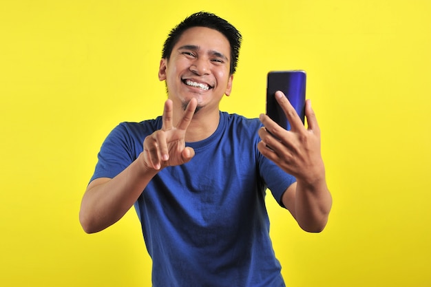 Heureux de beau jeune homme asiatique souriant à l'aide de smartphone isolé sur fond jaune