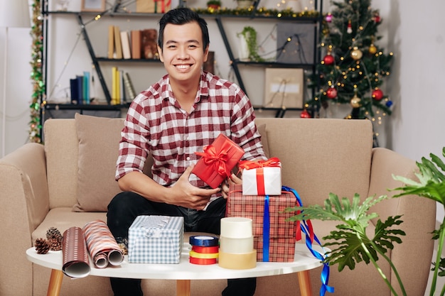 Heureux beau jeune homme vietnamien emballant des cadeaux de Noël pour des amis ou des membres de la famille