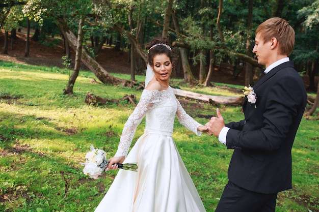 Heureux beau marié et belle mariée en robe blanche en riant et en dansant dans le parc