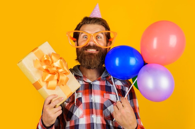 Photo heureux beau mec célébrant l'anniversaire de l'homme barbu en casquette de vacances avec des ballons et une boîte à cadeaux