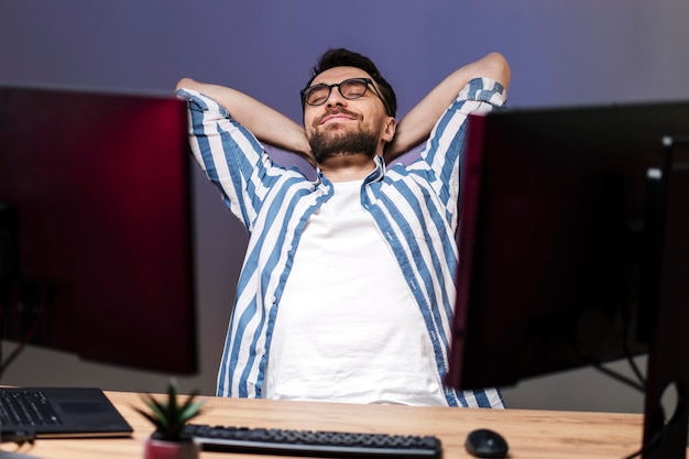 Heureux beau pigiste penché en arrière relaxant ayant une pause assis sur le lieu de travail