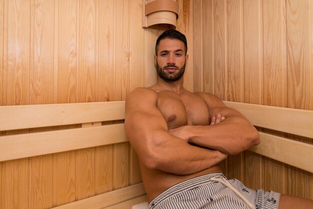 Photo heureux beau et séduisant jeune homme avec un corps musclé relaxant dans un sauna chaud