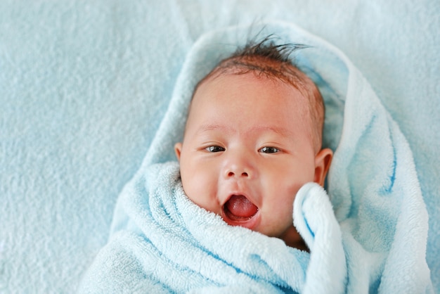 Heureux bébé garçon en rouleau de serviette allongé sur le lit après le bain