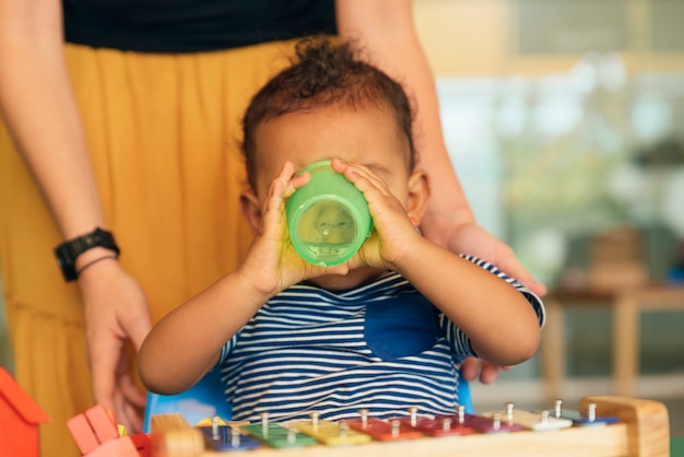 Heureux bébé qui boit de l'eau et joue avec des blocs de jouets à la maternelle.