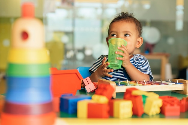 Heureux bébé qui boit de l'eau et joue avec des blocs de jouets à la maternelle.