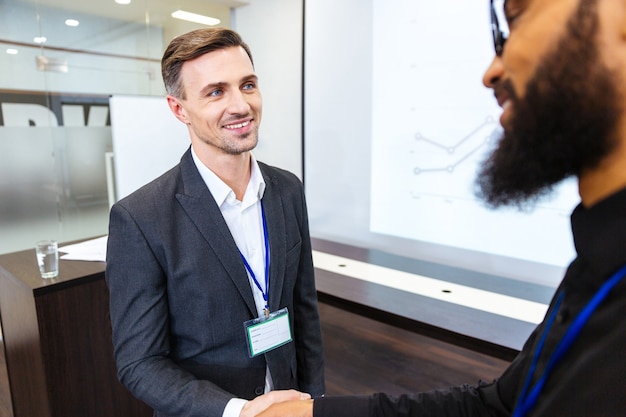 Heureux bel homme d'affaires serrant la main d'un jeune collègue africain barbu au bureau