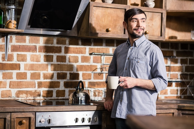 Heureux bel homme de boire du thé à la maison tout en profitant de l'heure du matin