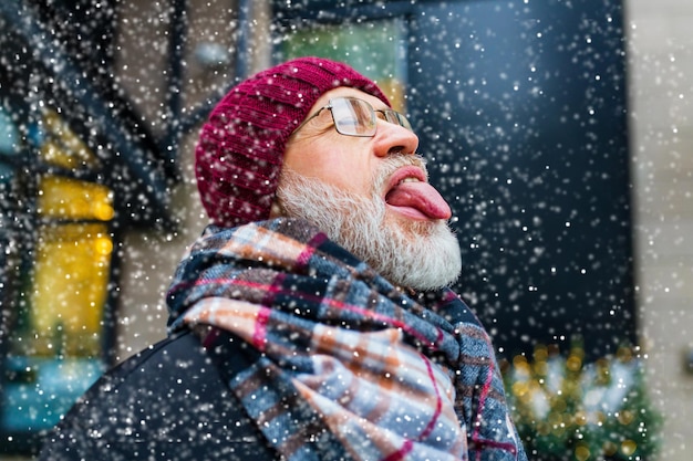 Heureux bel homme mûr qui sort sa langue attrape des flocons de neige dans la ville ville