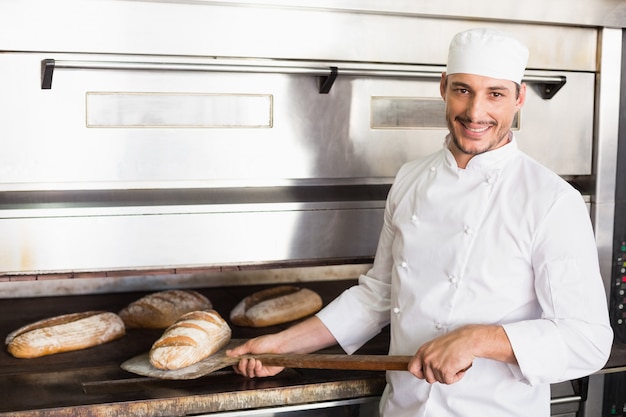 Heureux boulanger sortant du pain frais dans la cuisine de la boulangerie