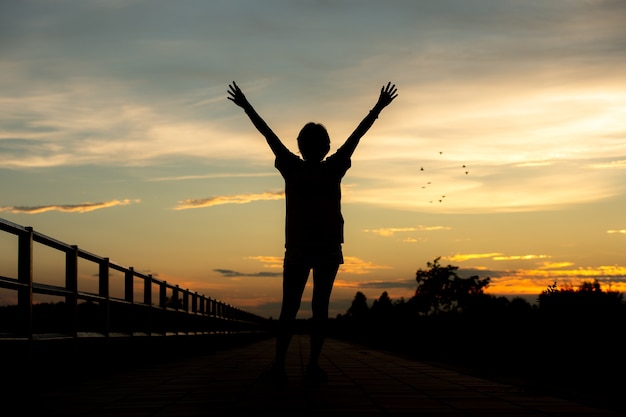 Heureux de célébrer la réussite de la femme au coucher du soleil ou au lever du soleil debout exalté avec les bras levés.