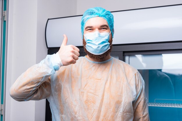 Heureux chef homme dans la cuisine montrant le pouce vers le haut pendant le covid-19