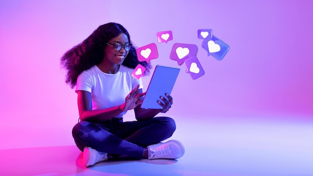 Heureux choqué jeune femme afro-américaine à lunettes a une conversation romantique avec des coeurs sur tablette