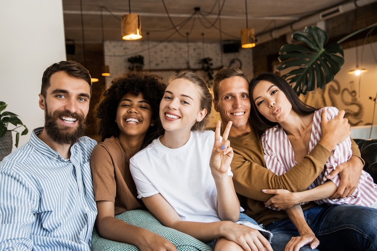 Photo heureux cinq amis dans un magasin de café souriant à la caméra faisant une photo de groupe
