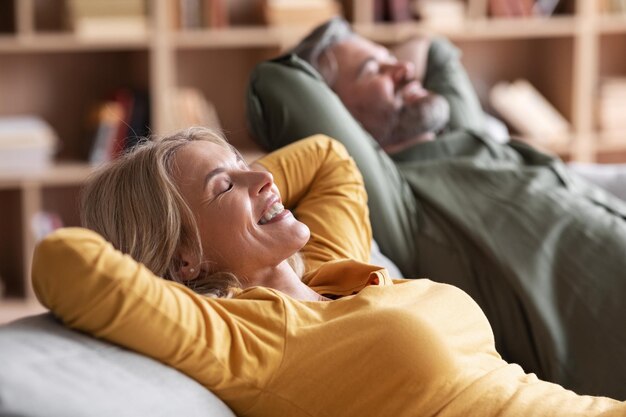 Photo heureux conjoints d'âge moyen détendu se penchant en arrière sur un canapé confortable