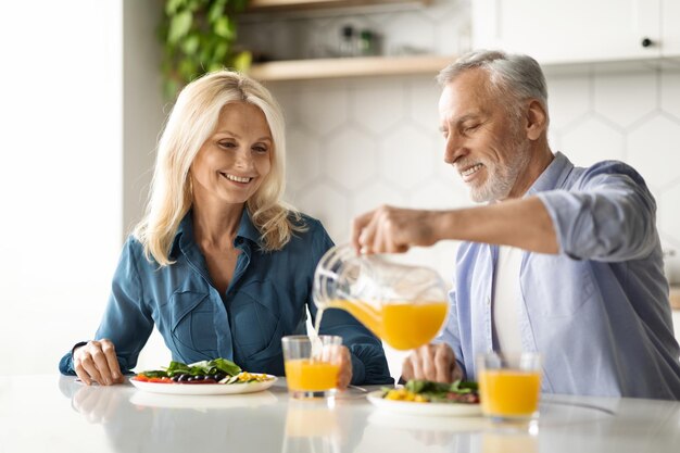 Heureux conjoints âgés mangeant un délicieux petit déjeuner ou déjeuner sain dans la cuisine