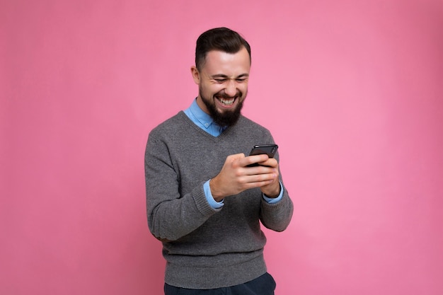 Heureux cool beau jeune homme non rasé brunet avec barbe portant un pull gris