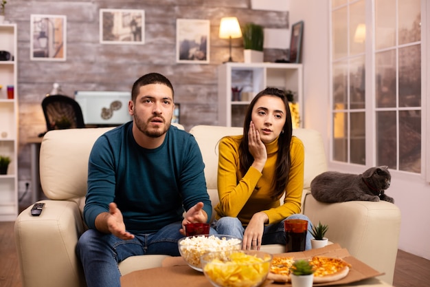 Heureux couple acclamant leur équipe préférée en regardant la télévision dans le salon.