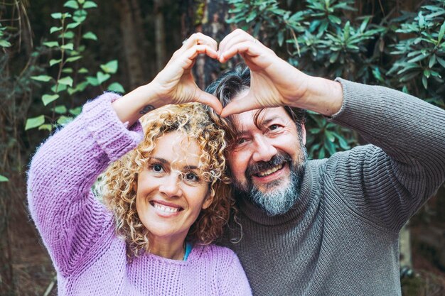 Heureux couple adulte amoureux font un geste de symbole de foyer avec les mains ensemble souriant et appréciant la relation Homme et femme loisirs avec feuillage vert bois forêt en arrière-plan