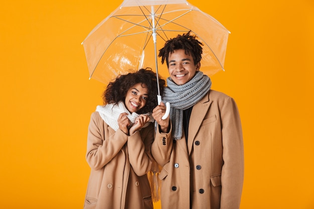 Heureux couple africain portant des vêtements d'hiver debout sous un parapluie isolé