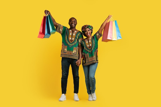 Heureux couple afro-américain en costumes nationaux tenant des sacs à provisions