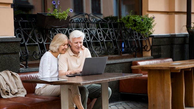 Heureux couple âgé assis sur un banc à l'extérieur avec ordinateur portable