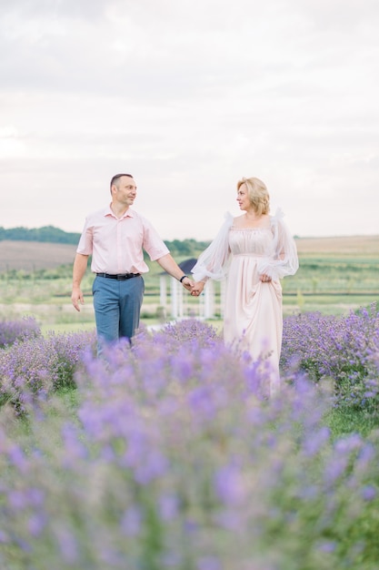 Heureux couple d'âge moyen marchant dehors dans le champ de floraison de lavande