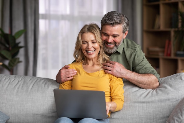 Heureux couple d'âge moyen avec ordinateur portable s'amusant ensemble à la maison