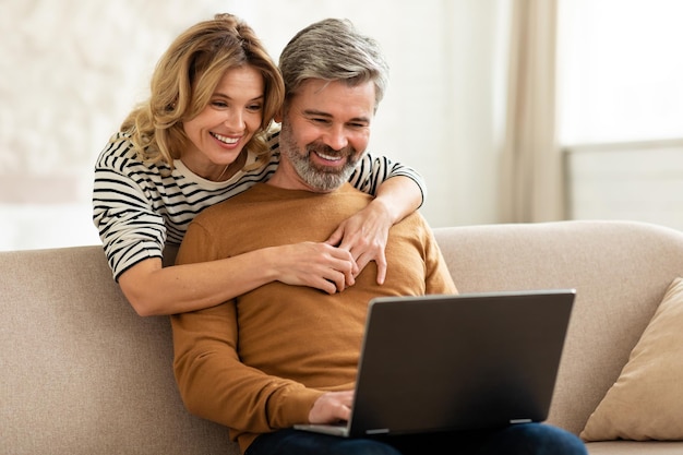 Heureux couple d'âge moyen utilisant un ordinateur portable naviguant sur Internet à la maison