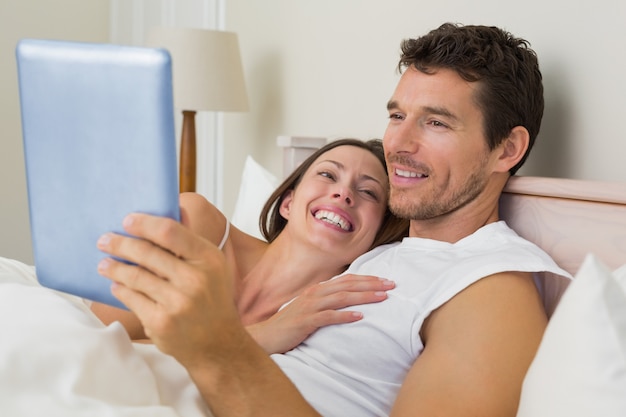 Heureux couple à l&#39;aide de tablette numérique dans son lit