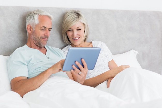 Photo heureux couple à l'aide de tablette numérique dans son lit