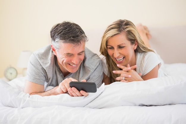 Heureux couple allongé sur le lit et regarder un téléphone mobile