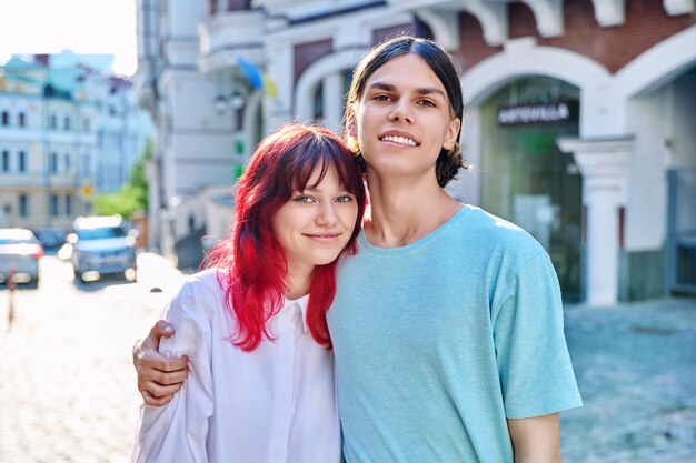 Heureux couple d'amis adolescents étreignant en regardant la caméra dans la rue de la ville