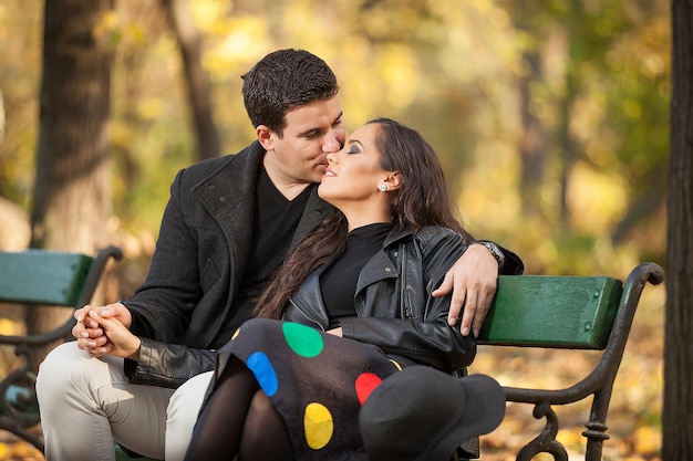 Heureux couple amoureux assis sur un banc dans le parc d'automne