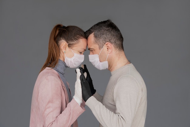 Heureux couple amoureux dans des masques et des gants de répétition étreignant isolé sur fond gris avec espace de copie. L'homme et la femme se tiennent la main pendant l'épidémie