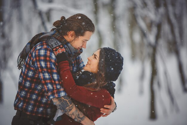 Heureux couple d'amoureux marchant dans la forêt enneigée