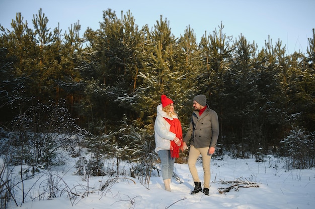 Heureux couple d'amoureux marchant dans la forêt d'hiver enneigée, passant des vacances de Noël ensemble. Activités saisonnières en plein air. Capture de style de vie.