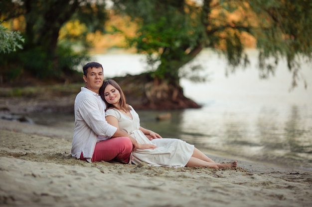 Heureux couple amoureux mari et femme sont assis sur une promenade sur le sable au bord de la rivière en été en vacances.