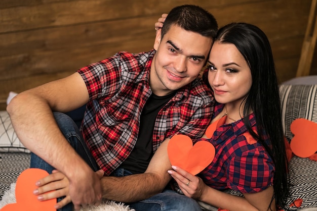 Heureux couple amoureux se serrant les uns les autres près du mur en bois dans un appartement avec un intérieur moderne Tenant le coeur rouge parer Love story concept