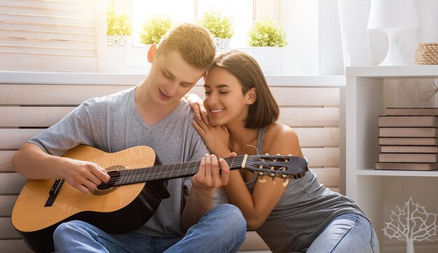 Heureux couple amoureux. Superbe portrait sensuel d'un jeune couple de mode élégant à l'intérieur. Jeune homme jouant de la guitare pour sa fille bien-aimée.