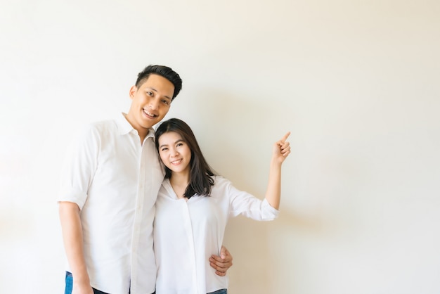 Heureux couple asiatique doigt pointé à l'espace de la copie vide sur le mur