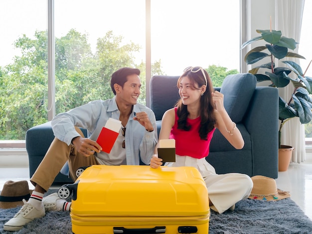 Heureux couple asiatique prêt à trébucher jeune homme et femme sourire et lever le poing et tenir et montrer le passeport ensemble près des bagages jaunes dans le salon se préparant à voyager en vacances vacances d'été