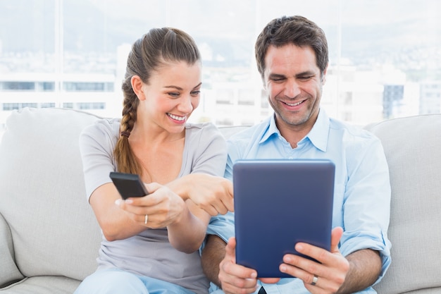 Heureux couple assis sur le canapé à l&#39;aide de tablet pc et regarder la télévision