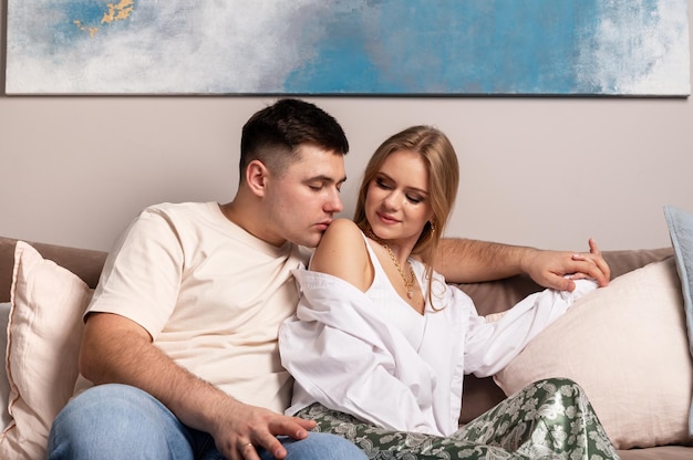 Heureux couple assis sur un canapé à la maison bel homme embrassant une belle femme sur l'épaule avec tendresse