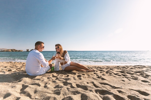 Heureux couple assis avec champagne sur la plage