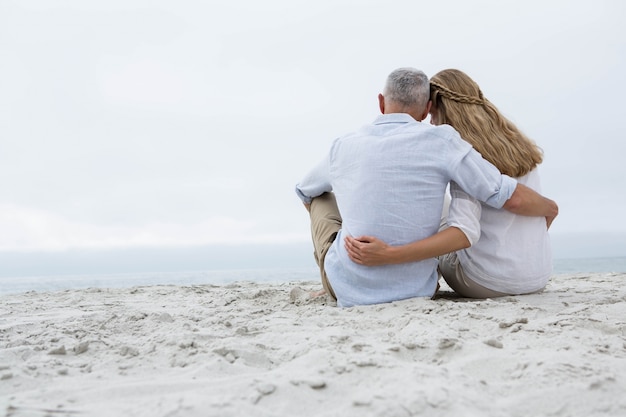 Heureux couple assis sur le sable et en regardant la mer