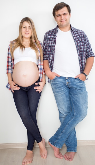 Heureux couple en attente de bébé posant en jeans et chemises