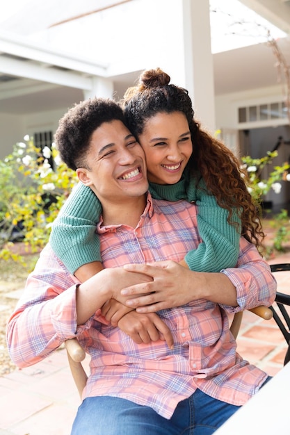 Heureux couple biracial sur la terrasse du jardin embrassant l'extérieur de la maison en souriant. Concept d'inclusivité, de vie domestique, de loisirs, de romance et de convivialité.