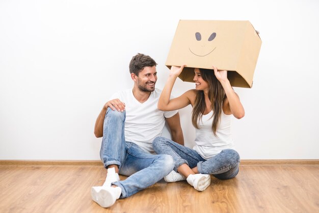 L'heureux couple avec une boîte en carton est assis sur le sol